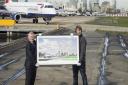 Artist Gerry Buxton holds his artwork with London City Airport boss DEclan Collier as a plane taxis on the runway matching the image in the screen-print. Picture: LCY/Gerry Buxton